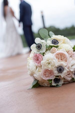 Elegant wedding bouquet with white anemones and blush roses with couple in background.