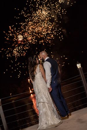Bride and groom share a kiss with spectacular fireworks display lighting the night sky.