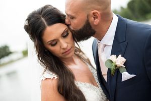 Groom tenderly kissing bride on the cheek during romantic outdoor wedding portrait near water.