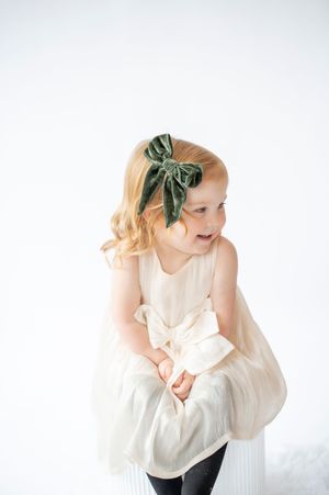 Adorable little girl in cream dress with green velvet bow laughing in white studio.