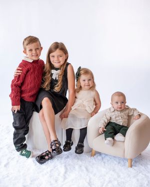 Four young siblings posing together in holiday outfits on white studio background.