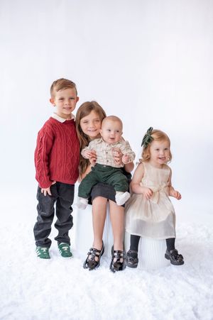 Four children in festive holiday outfits posing together on white snowy studio background.