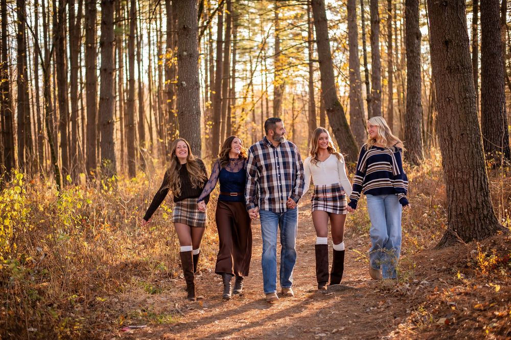 Five friends walk together on a sunlit autumn forest trail surrounded by golden fall foliage.