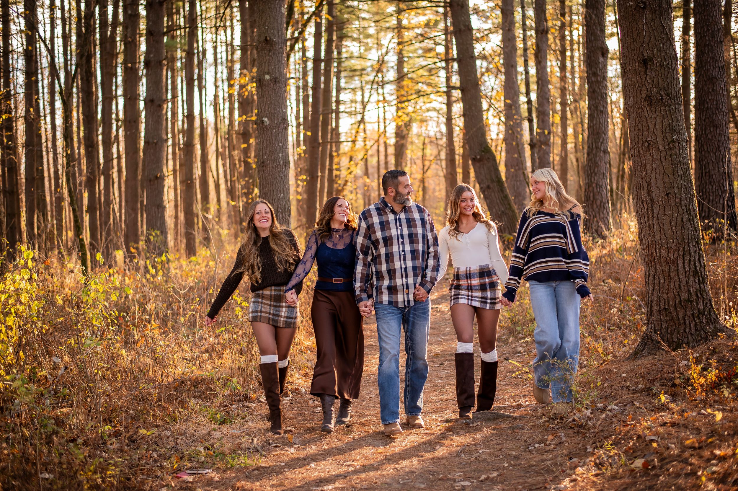 Five friends walk together on a sunlit autumn forest trail surrounded by golden fall foliage.