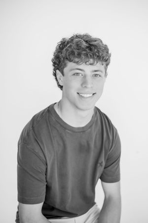 Black and white portrait of a smiling teenage boy with curly hair wearing a t-shirt.