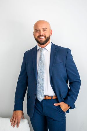 Bald man with beard in navy blue suit and tie smiling in professional portrait.