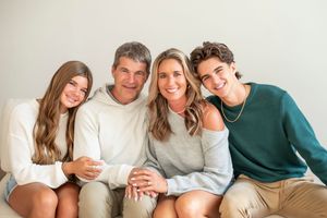 Smiling family of four posing together on couch in bright modern home setting.