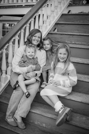 Black and white portrait of a mother sitting on porch steps with her three young daughters.