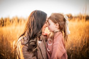 Mother and young daughter touching foreheads tenderly in a golden autumn wheat field.