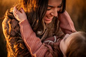 Smiling mother gazes lovingly at her child in a warm golden field at sunset.