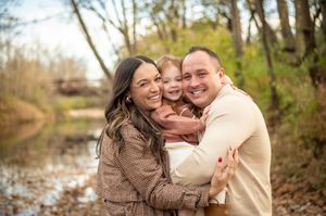 Happy family with young child embracing outdoors near creek in autumn forest setting.