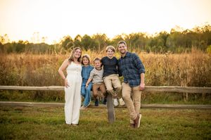 Happy family of five poses at a wooden fence in a golden field at sunset.