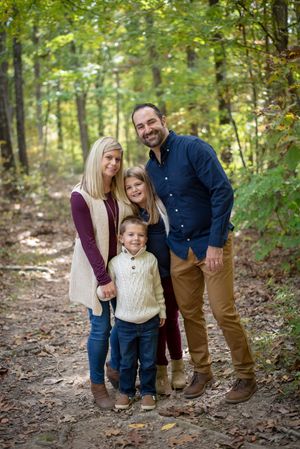 Happy family of four posing together on a forest trail surrounded by autumn foliage.