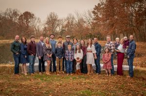 Large extended family group portrait outdoors among colorful autumn foliage near pond.