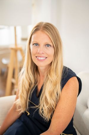 Smiling blonde woman with blue eyes seated on a sofa in a bright airy room.