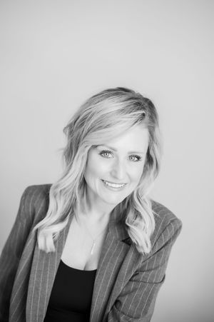 Black and white portrait of a smiling blonde woman in a pinstripe blazer.