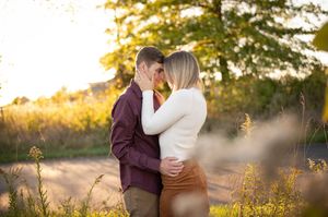Couple shares a tender moment kissing in golden sunlit field during engagement session.