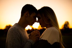 Couple holds hands and touches foreheads in intimate golden sunset engagement portrait.