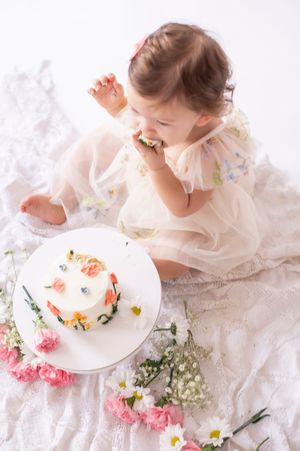 Overhead view of a baby girl in a sheer dress eating her floral first birthday smash cake.