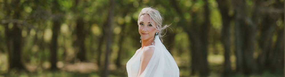 A person in a white wedding dress poses outdoors in a wooded setting with soft natural lighting.