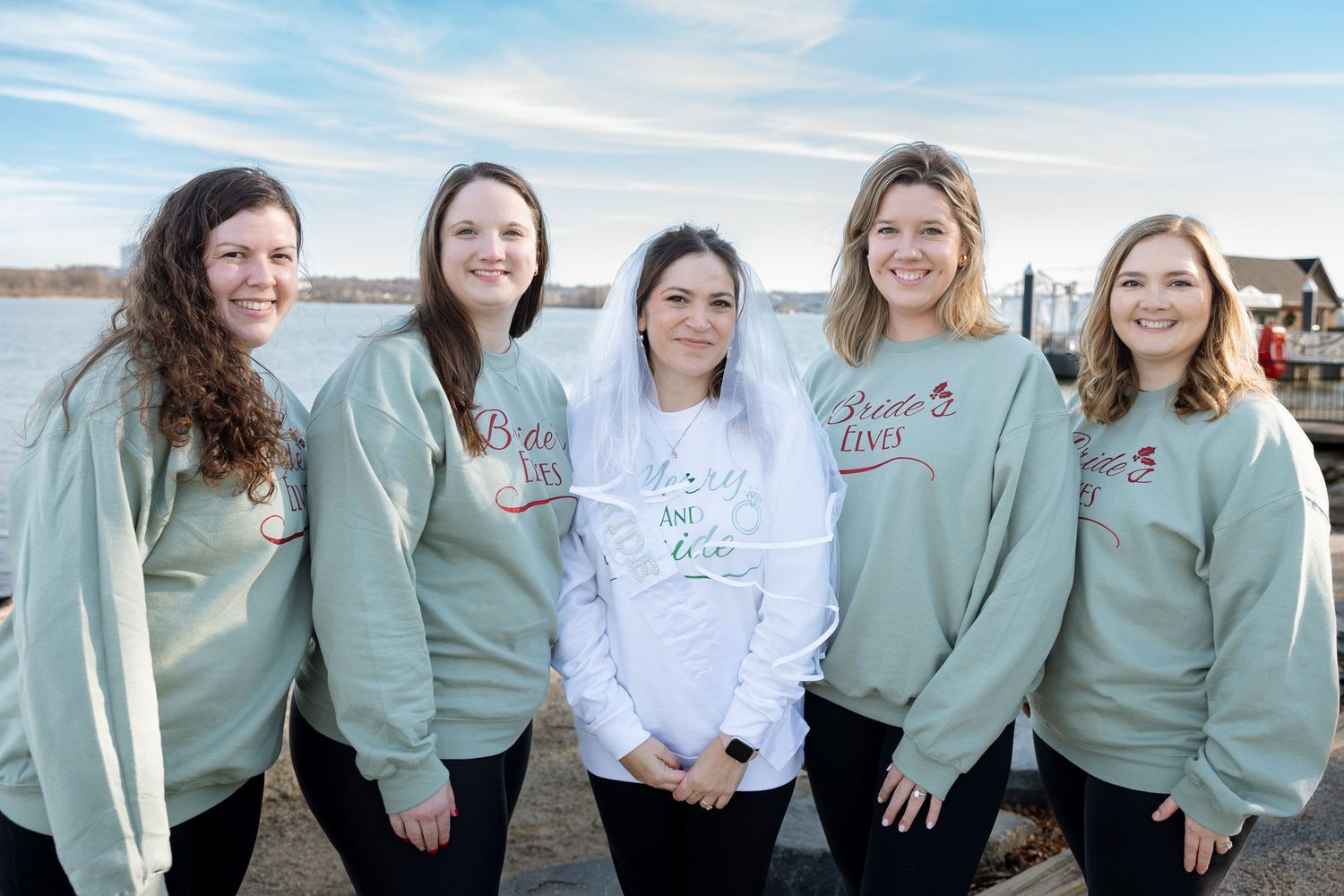 Bride surrounded by bridesmaids wearing matching sweatshirts — candid wedding celebration portrait