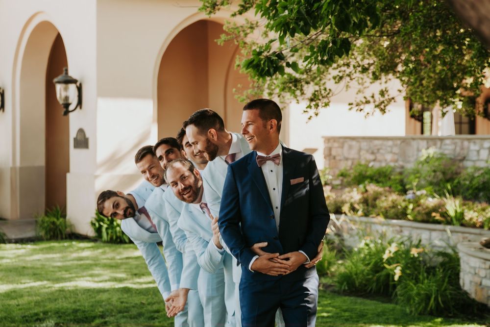 Wedding party gathered under stone archways in an outdoor garden setting during a sunny afternoon celebration.