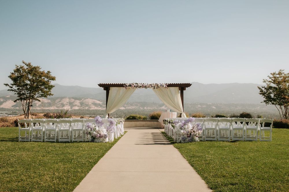 Panoramic view of white wedding chairs arranged in rows on a grassy field with mountains in the background.