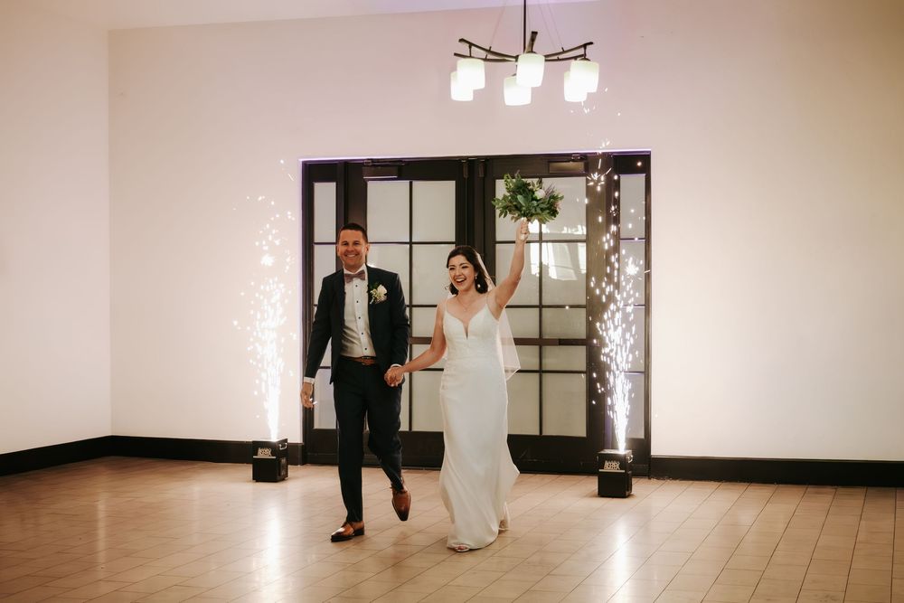 A couple makes their grand entrance through French doors at their wedding reception venue.