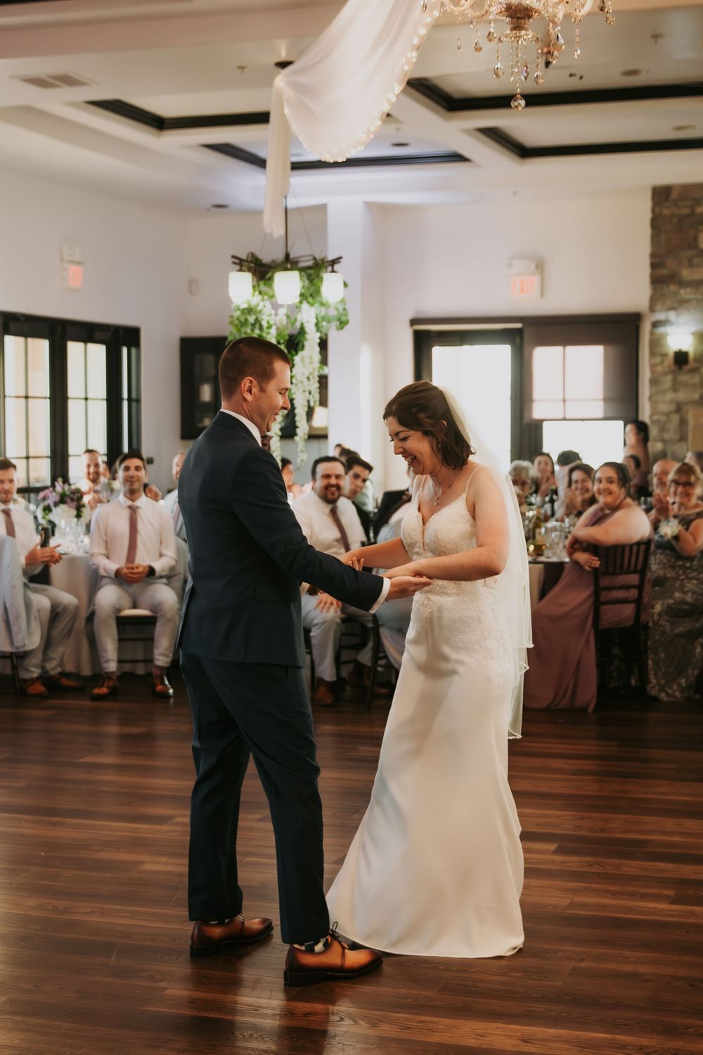 Newlyweds share their first dance on a polished hardwood floor in an elegant reception venue.