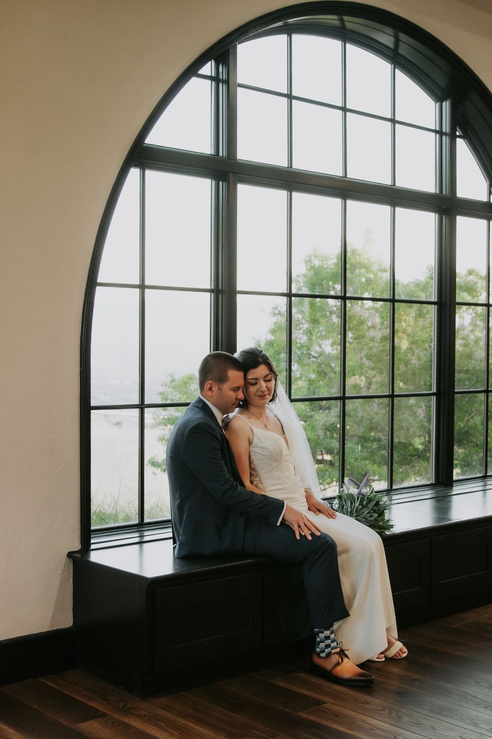 A romantic moment captured by an arched window with a couple sitting together on a bench.
