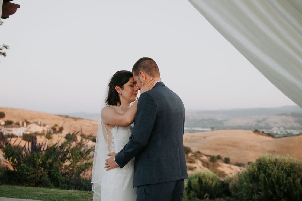 A romantic outdoor wedding moment with flowing white curtains and rolling hills in the background.