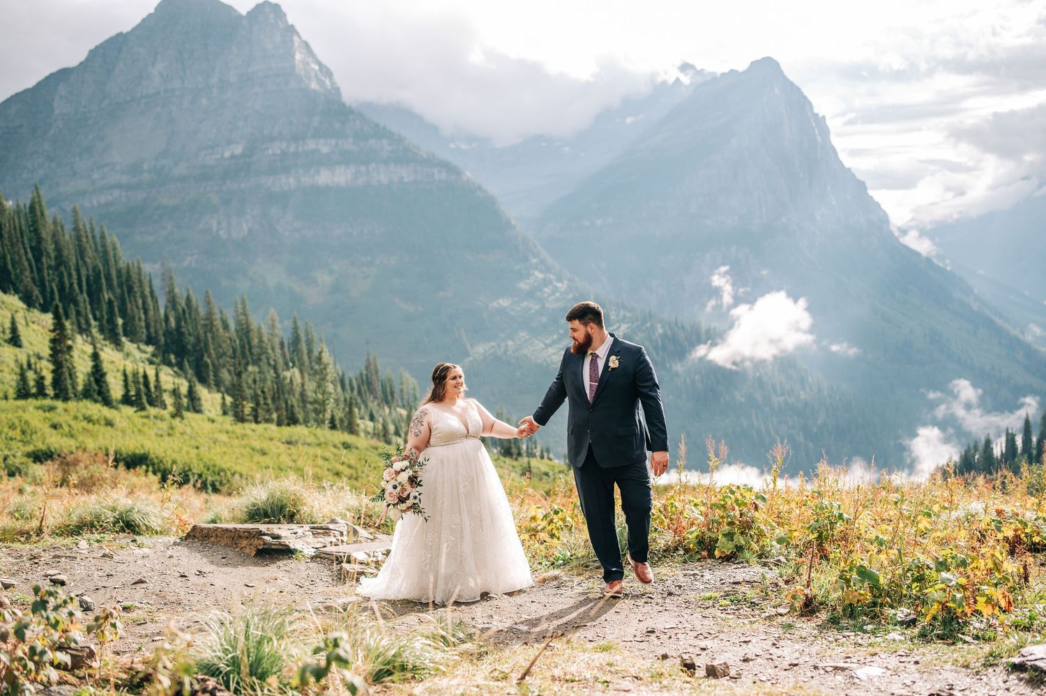 Couple walking through wildflower meadows at Big Bend with majestic mountain peaks and glaciers in the backdrop at sunset.