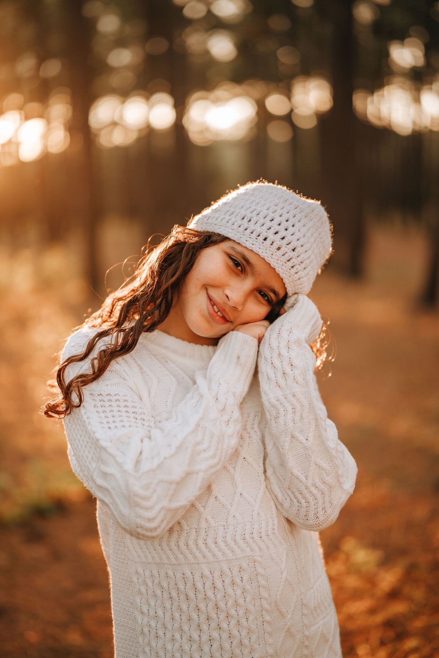 Portrait in cozy white knit sweater and beanie against golden autumn forest bokeh background.