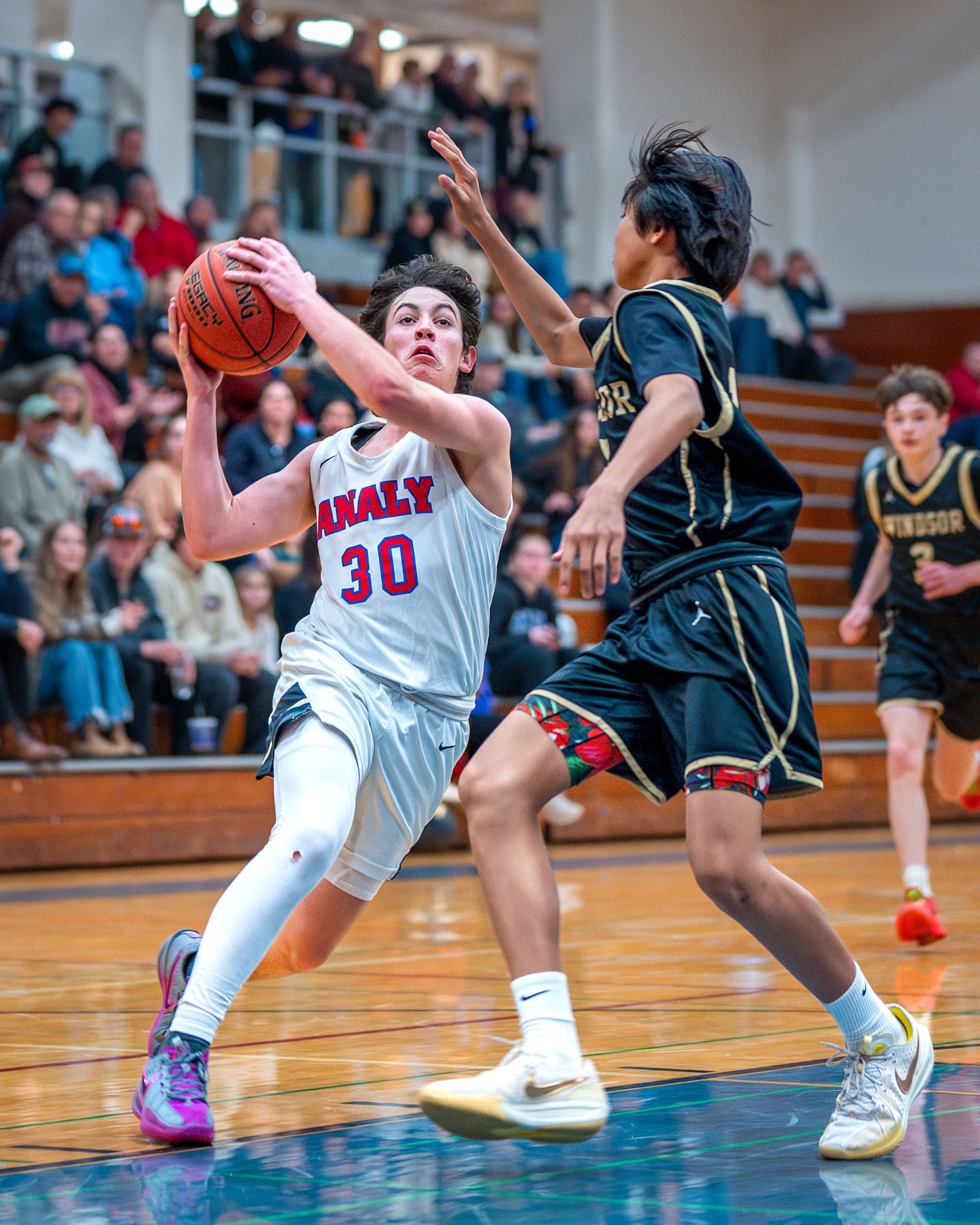 High school basketball players compete for the ball during an intense game in a packed gymnasium.