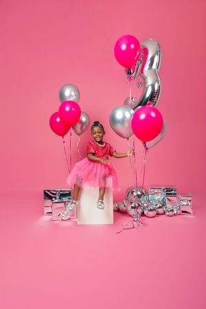 Birthday celebration setup with pink and silver balloons, cake, and tulle dress against pink backdrop.