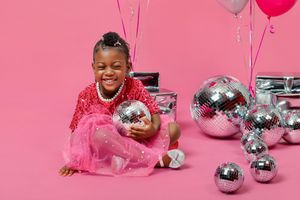 Festive scene with metallic balloons, disco balls, and pink decorations arranged on a pink background.