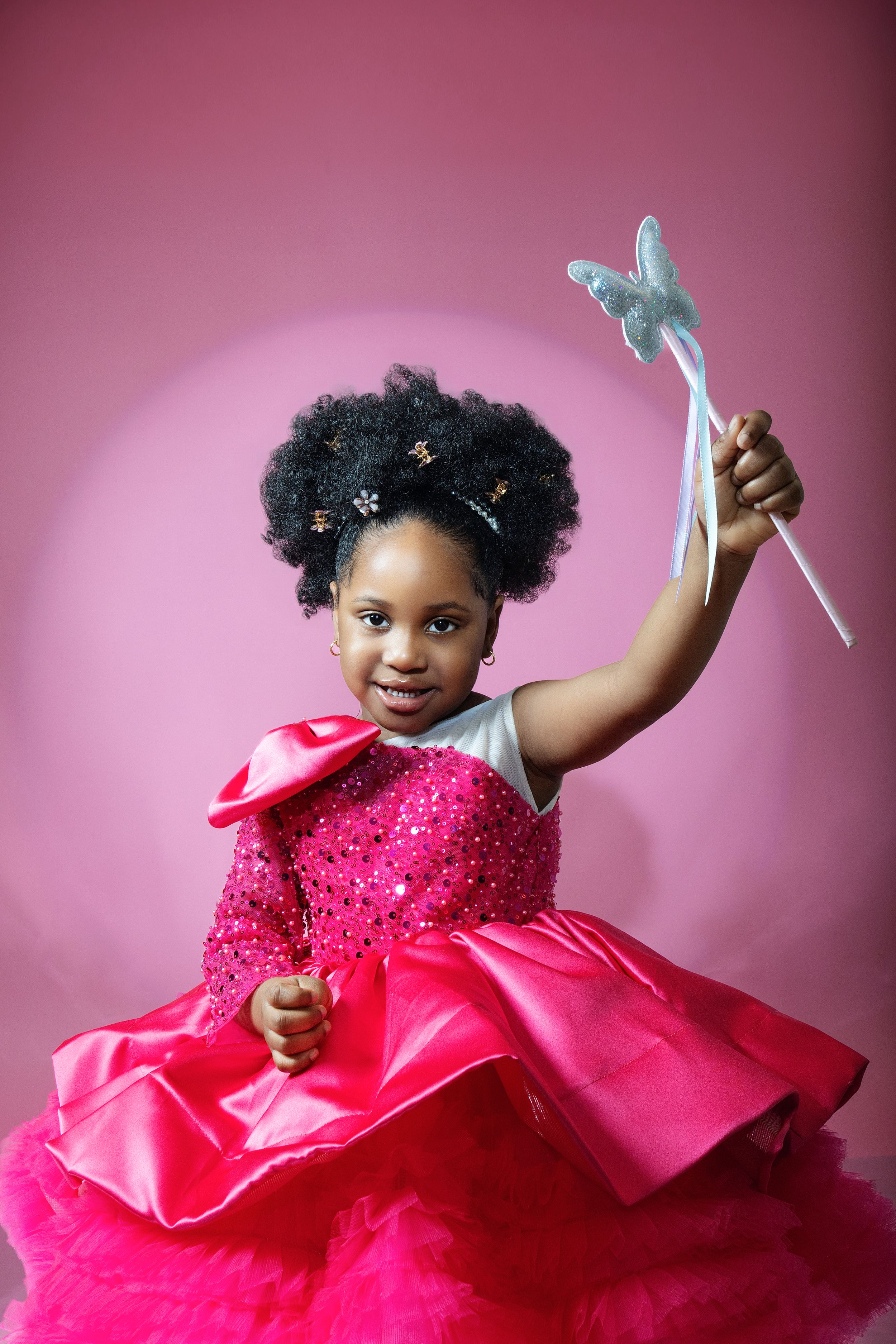 Playful child in sparkly pink dress throwing shoes during holiday photoshoot.