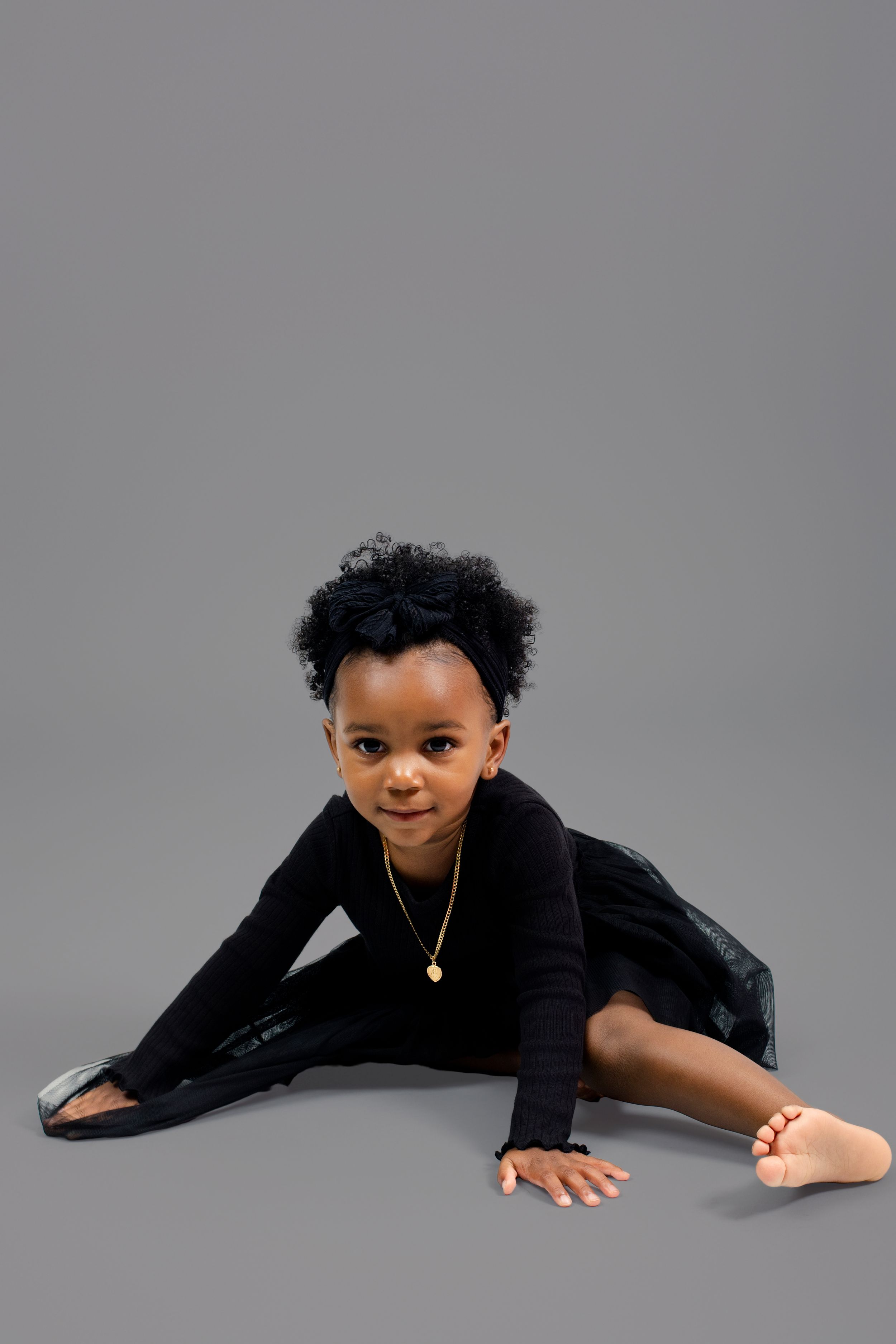 Child in black sweater lying on gray studio floor during portrait session.