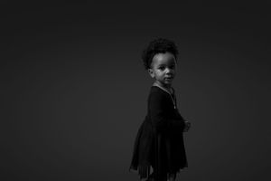 Dramatic black and white studio portrait of child in dark dress.