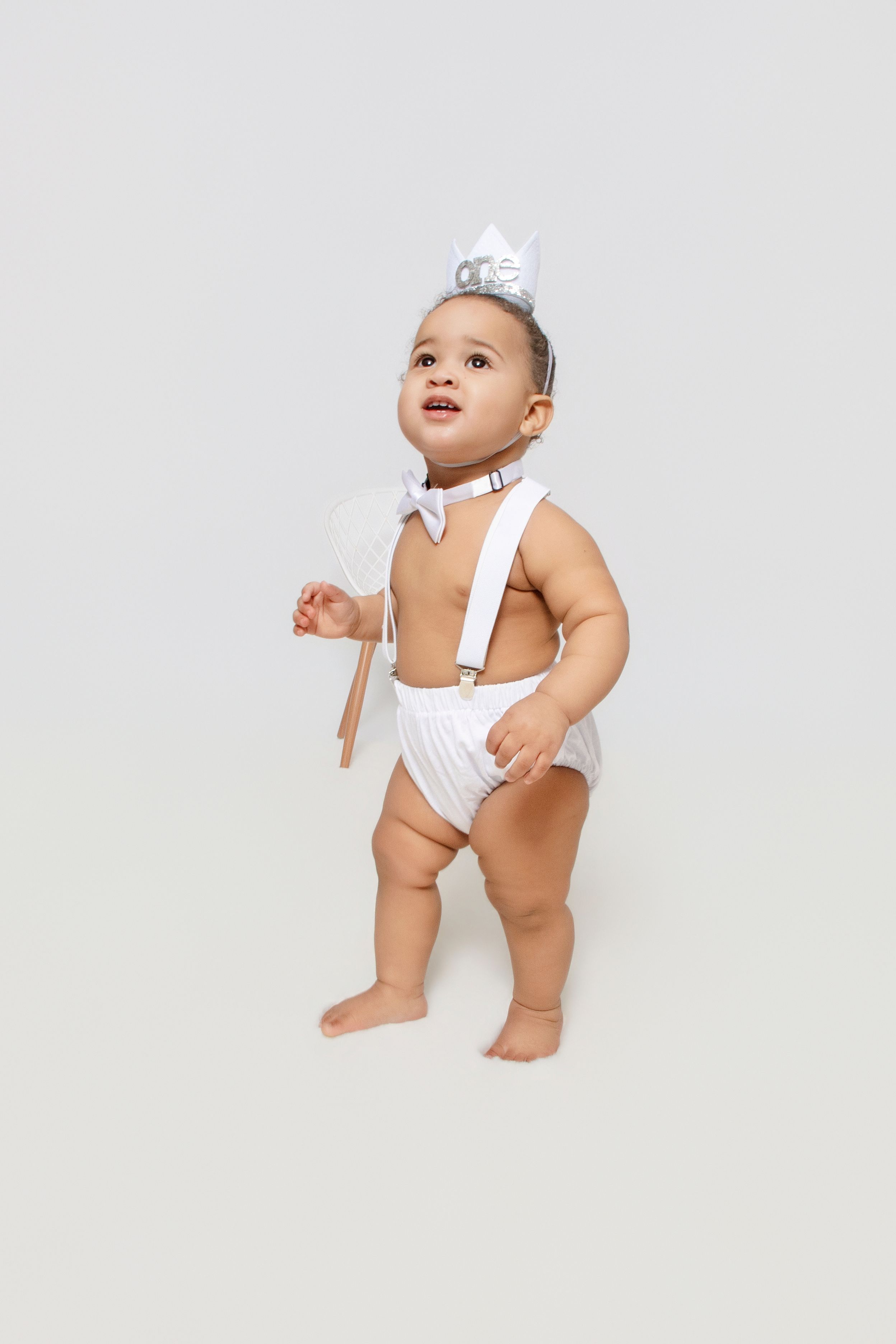 Baby in white outfit crawls and plays on white background.