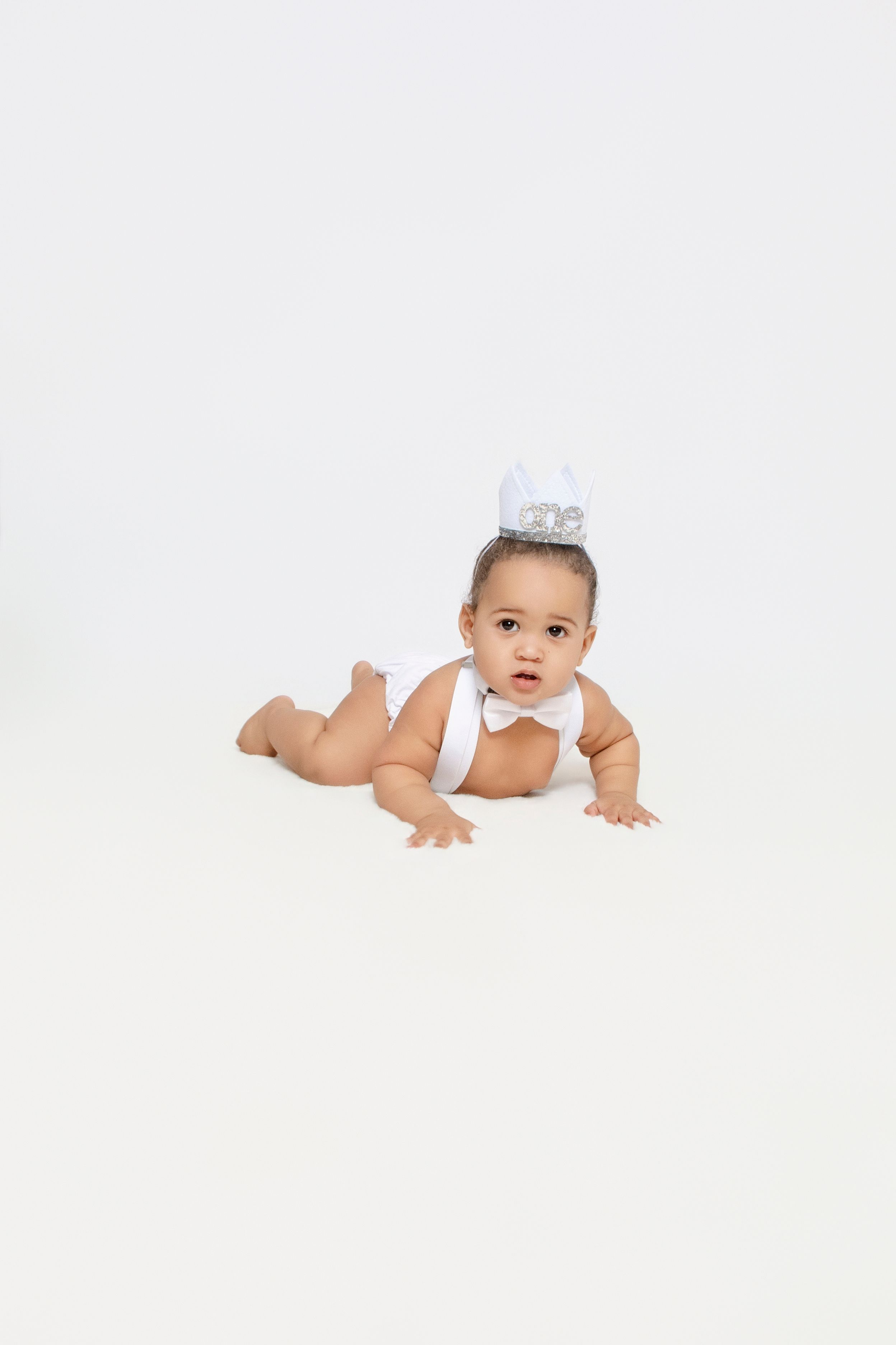 Baby wearing bow tie crawls on white studio floor.