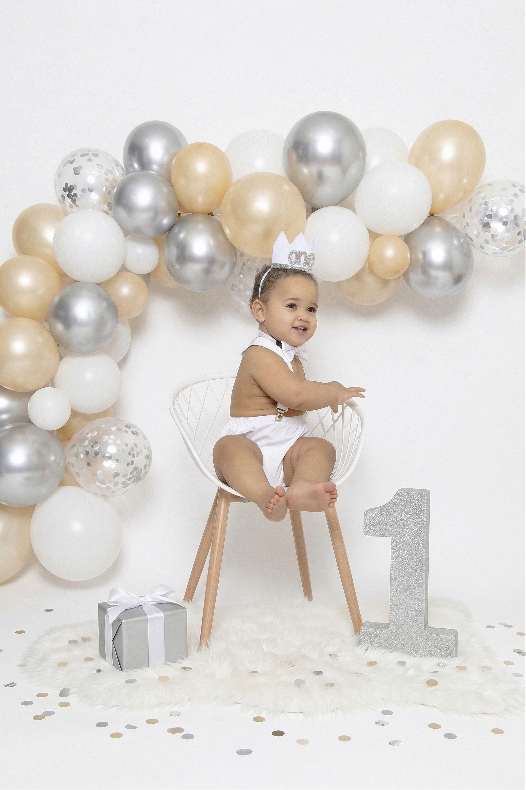 Baby's first birthday photo with balloon arch and modern chair setup.