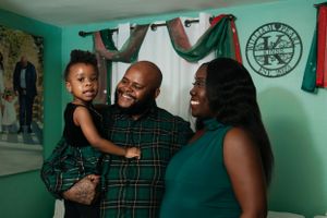 Family of three smiling together in room with teal walls and holiday decorations.