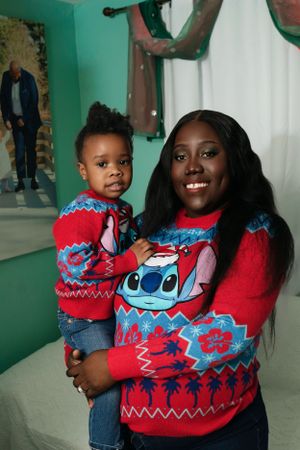 Two people wearing matching Christmas sweaters smiling together in festively decorated room.