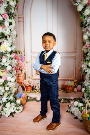 Studio portrait setup with navy vest and brown shoes against a floral backdrop with pink accents.