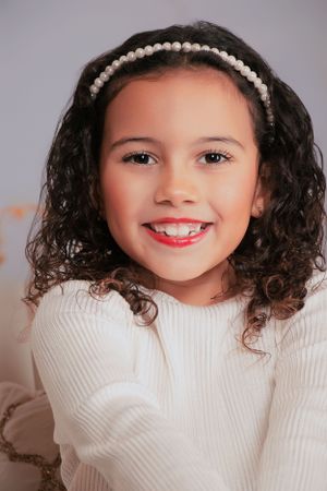 Winter portrait with pearl headband and white knit sweater against neutral background.