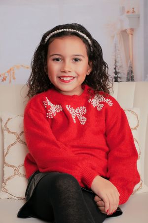 Holiday portrait featuring red sweater with bow details and black pants against winter decor.