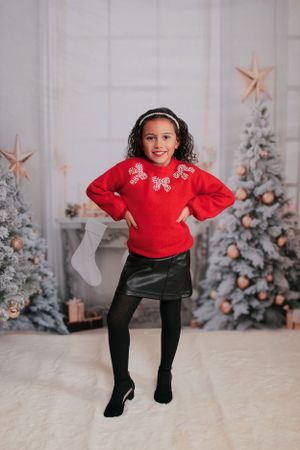 Playful pose in red sweater and black skirt with Christmas decorations in background.