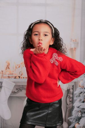 Energetic pose in bright red holiday sweater with decorative bow detail.