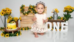 Sunflower themed first birthday photo setup with wooden backdrop and rustic decorations.